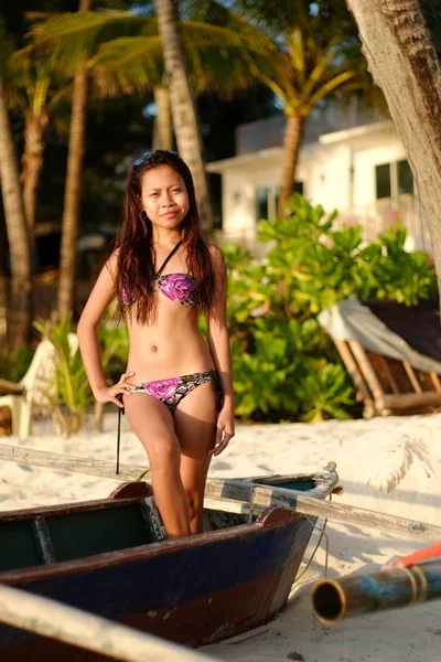 Menina bonita feliz em um maiô de verão sentado em um velho barco de pesca na praia de areia branca tropical. Conceito férias de verão — Fotografia de Stock