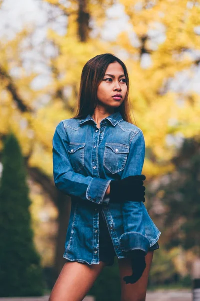 Wanita muda cantik mengenakan jaket jeans biru dengan perbukitan tinggi dan kaus kaki panjang bergaris-garis lutut. Gadis yang duduk di taman — Stok Foto