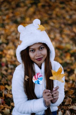  Sonbahar güneşli parkta genç kadın gülümseyerek, yaprakları ve şeker. Beyaz kazaklı neşeli güzel kız
