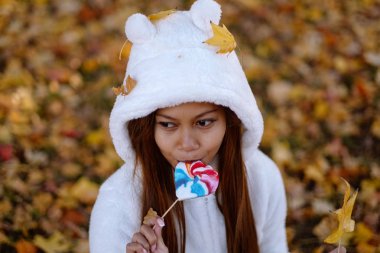  Sonbahar güneşli parkta genç kadın gülümseyerek, yaprakları ve şeker. Beyaz kazaklı neşeli güzel kız