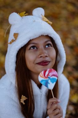  Sonbahar güneşli parkta genç kadın gülümseyerek, yaprakları ve şeker. Beyaz kazaklı neşeli güzel kız