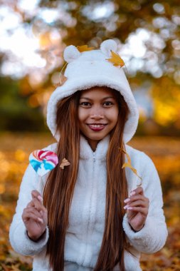  Sonbahar güneşli parkta genç kadın gülümseyerek, yaprakları ve şeker. Beyaz kazaklı neşeli güzel kız
