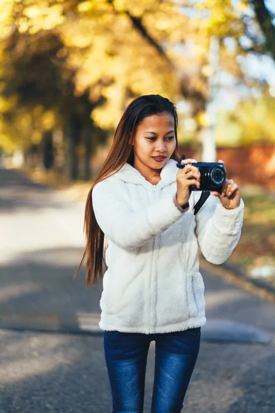 Beautiful girl in white woolen coat photographing outside on the street during autumn afternoon — Stock Photo, Image