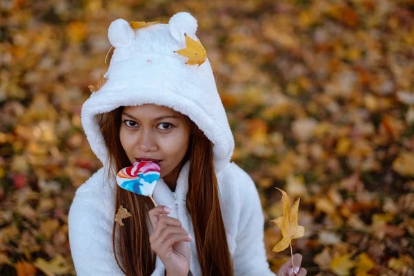  Sonbahar güneşli parkta genç kadın gülümseyerek, yaprakları ve şeker. Beyaz kazaklı neşeli güzel kız