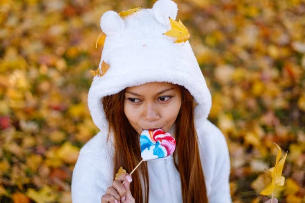 Sonbahar güneşli parkta genç kadın gülümseyerek, yaprakları ve şeker. Güzel renkli arka plan ile parkta beyaz kazaklı neşeli güzel kız