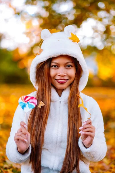 Sonbahar güneşli parkta genç kadın gülümseyerek, yaprakları ve şeker. Güzel renkli arka plan ile parkta beyaz kazaklı neşeli güzel kız