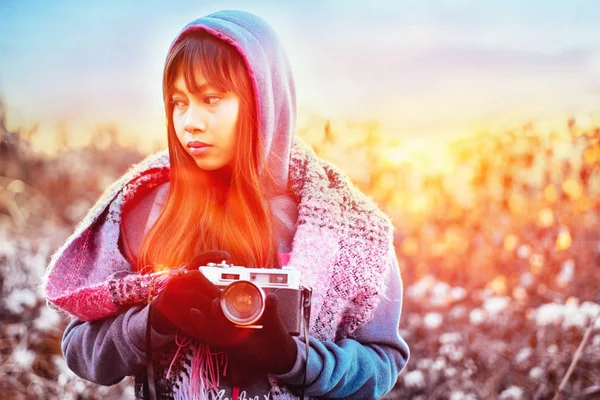 Genç kadın fotoğrafçı kazak ve renkli atkı öğleden sonra boyunca giyiyor soğuk havalarda dışarıda günbatımı