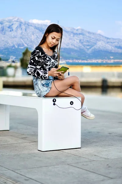 Beautiful woman charging her phone on free multipurpose solar panel charger incorporated in to sitting bench for cittisents.Modern technology free energy for everyone .