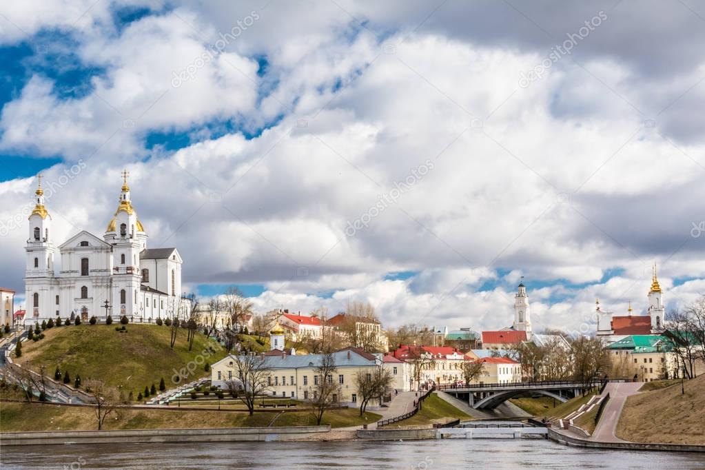 City architecture, on the bank of the river there is a Christian church, a monastery of the princess, a chapel / town hall, a small bridge connects two banks, footpaths, a sunny day, Belarus Vitebsk