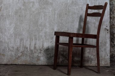 Loş bir ışık ile terk edilmiş, kasvetli bir odada bir beton zemin üzerinde çatlaklar ile eski yıpranmış sandalye olduğunu