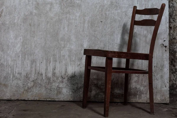 Vieja silla desgastada con grietas está en un piso de hormigón en una habitación abandonada y sombría con una luz tenue — Foto de Stock