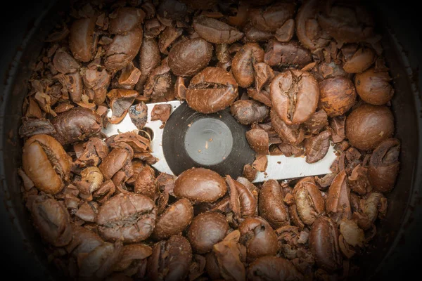 Partially ground fried dark coffee beans in an automatic coffee grinder, close-up food background — Stock Photo, Image