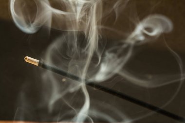 Koyu arka plan üzerinde duman ile yanan tütsü sopa