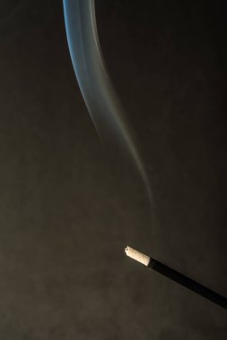 Koyu arka plan üzerinde duman ile yanan tütsü sopa
