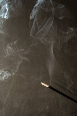 Koyu arka plan üzerinde duman ile yanan tütsü sopa
