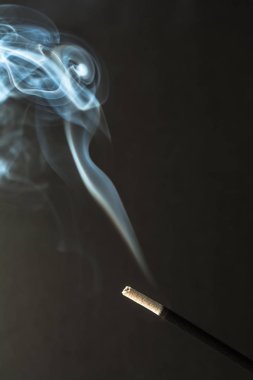 Koyu arka plan üzerinde duman ile yanan tütsü sopa