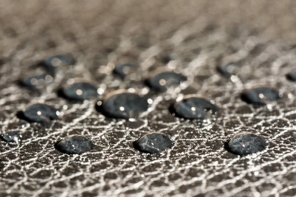 Gotas redondas escuras de água na superfície em relevo de couro preto, fundo macro — Fotografia de Stock