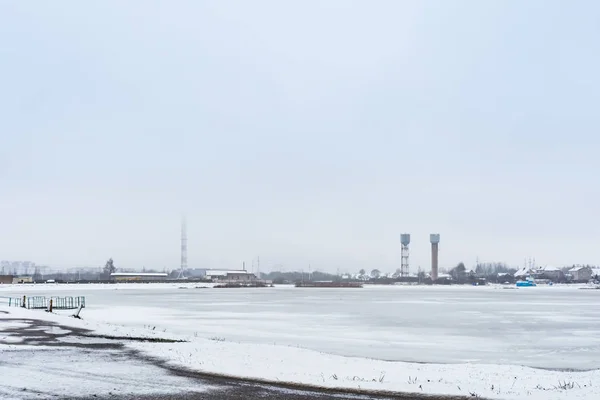 A lagoa é coberta com gelo, no horizonte de alta construção industrial, tempo nublado sombrio — Fotografia de Stock