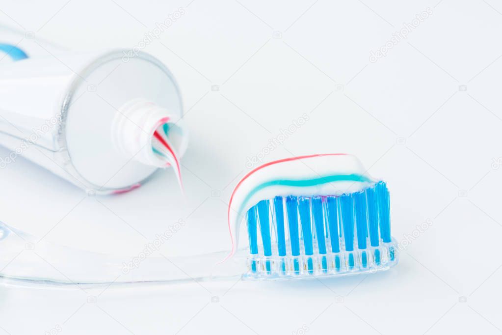 toothbrush of clear plastic with blue bristles, white blue red toothpaste squeezes out of a tube