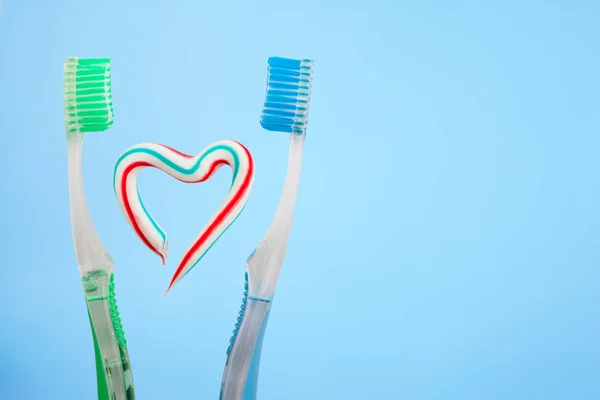 The heart symbol is made from a three-color toothpaste and is located between two toothbrushes — Stock Photo, Image