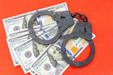 100 dolarlık banknotlar kırmızı bir arka plan üzerinde yatan siyah metal kelepçe