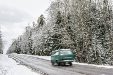 Ormanda, karlı kış yolu boyunca giden bir araba. Kışın bulutlu havada tehlikeli sürüş koşulları.