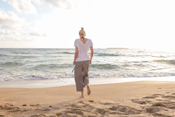 Mujer caminando en la playa de arena a la hora dorada —  Fotos de Stock