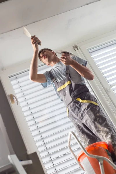 Yesero renovando paredes y techos interiores. Trabajos de acabado de construcción . — Foto de Stock