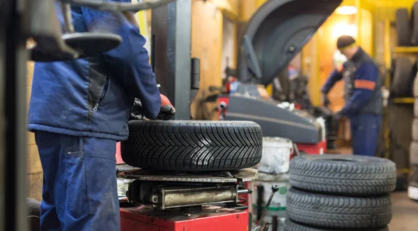 Professional auto mechanic replacing tire on wheel in car repair service. — Stock Photo, Image