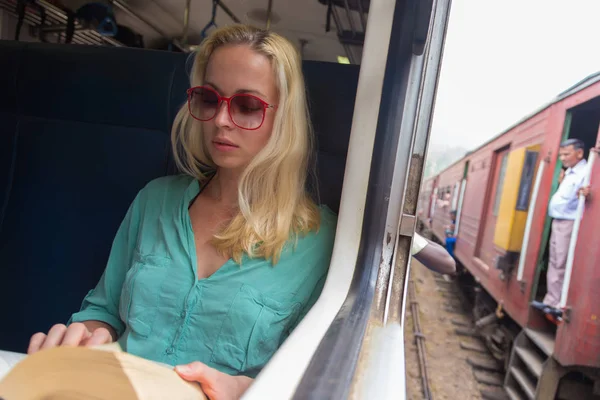 Rubia mujer caucásica leyendo libro en tren por la ventana . — Foto de Stock