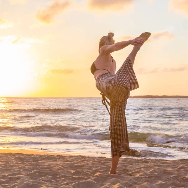 Kobieta ćwiczy jogę na plaży morskiej o zachodzie słońca. — Zdjęcie stockowe