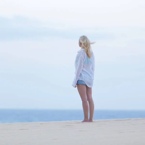 女人穿白衬衣，在黄昏的沙滩上. — 图库照片