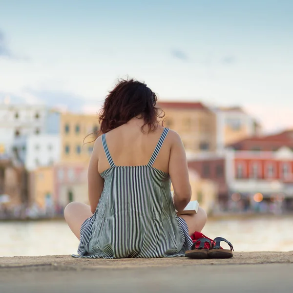 Achteraanzicht van een vrouw zitten op een pier, boek lezen. — Stockfoto