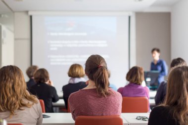 Üniversitedeki konferans salonunda sunum yapan kadın..
