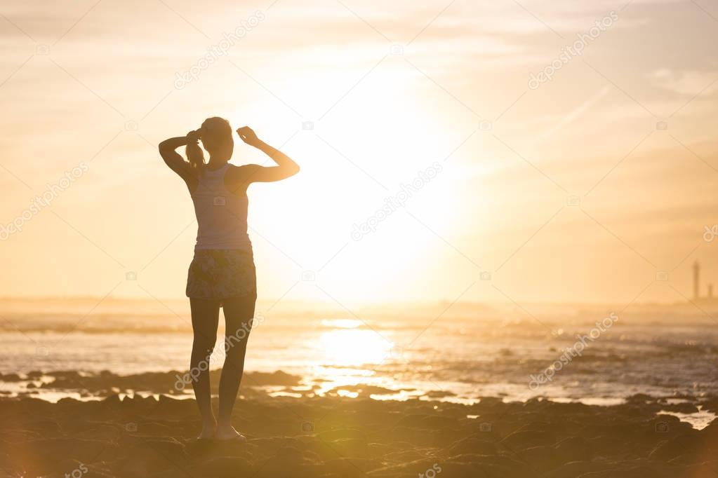 Woman on sandy beach watching sunset.