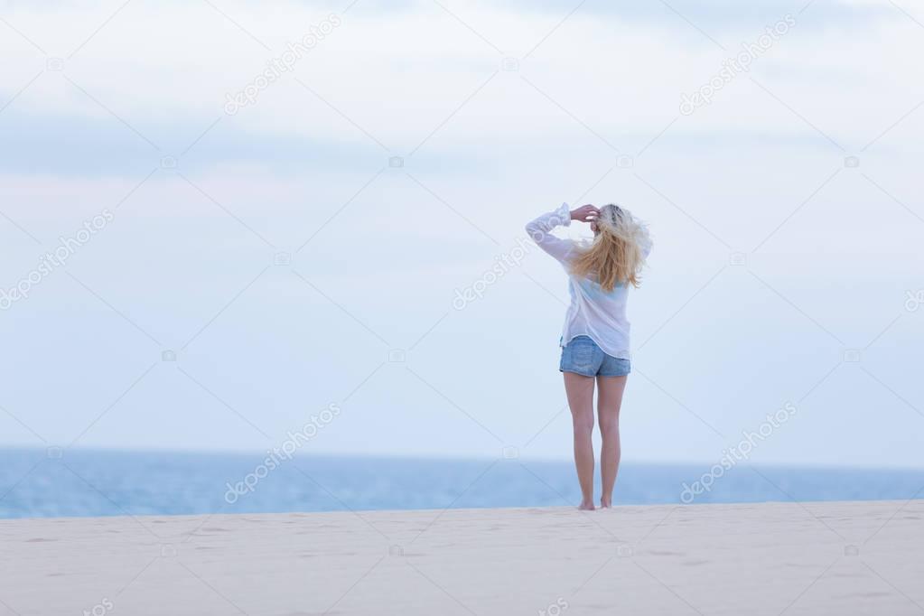 Woman on sandy beach in white shirt at dusk.