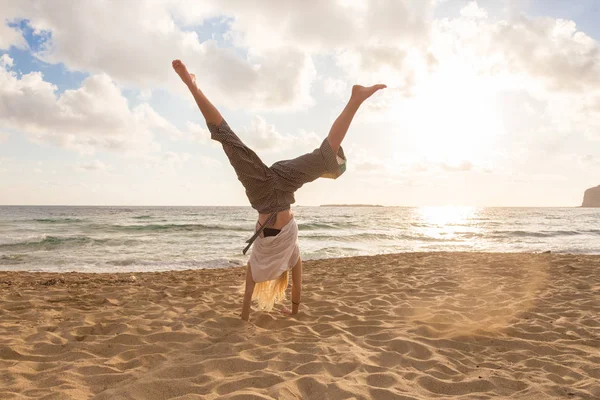 Freie glückliche Frau, die Wagenrad dreht und den Sonnenuntergang am Sandstrand genießt. — Stockfoto