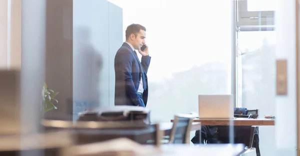 Biznesmen rozmawiający przez telefon komórkowy patrząc przez okno. — Zdjęcie stockowe