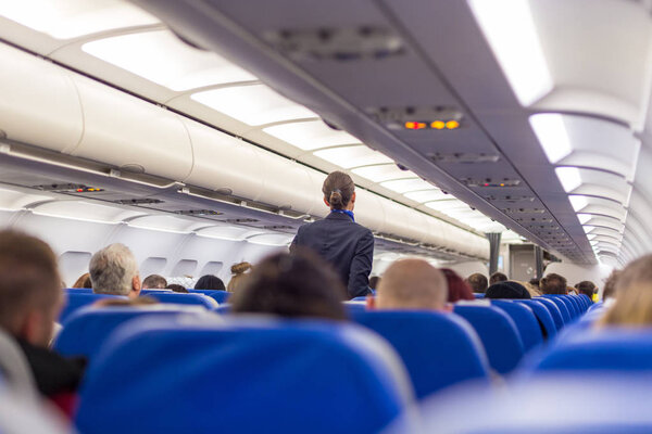 Stewardess walking the aisle of commercial airplane.