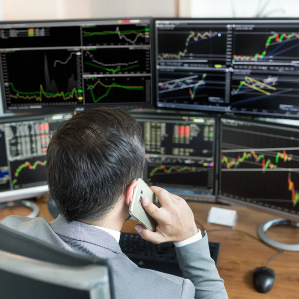 Over the shoulder view of stock broker trading online, talking on mobile phone. — Stock Photo, Image