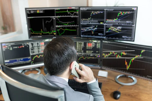 Over the shoulder view of stock broker trading online, talking on mobile phone. — Stock Photo, Image