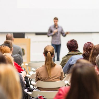 Üniversitedeki konferans salonunda sunum yapan adam.
