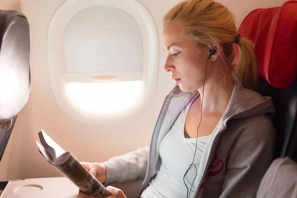 Woman reading magazine and listening to music on airplane. — Stock Photo, Image