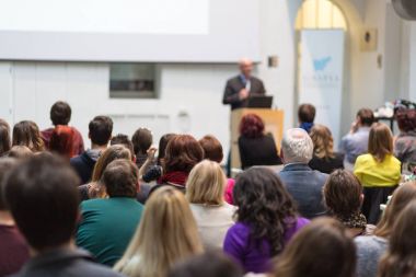 Üniversitedeki konferans salonunda sunum yapan adam.