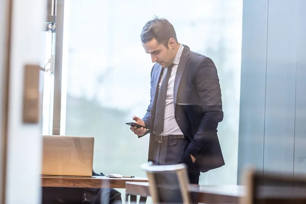 Бизнесмен смотрит на смартфон в современном корпоративном офисе . — стоковое фото