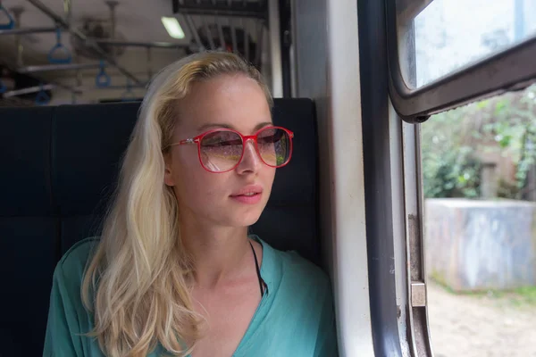Blonde femme caucasienne chevauchant un train, regardant par la fenêtre. — Photo