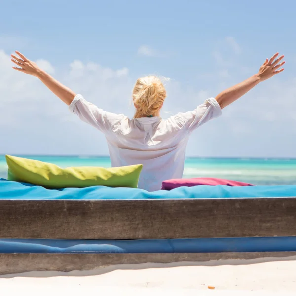 Mujer relajada en una tumbona de lujo, brazos levantados, disfrutando de las vacaciones de verano en la hermosa playa . — Foto de Stock