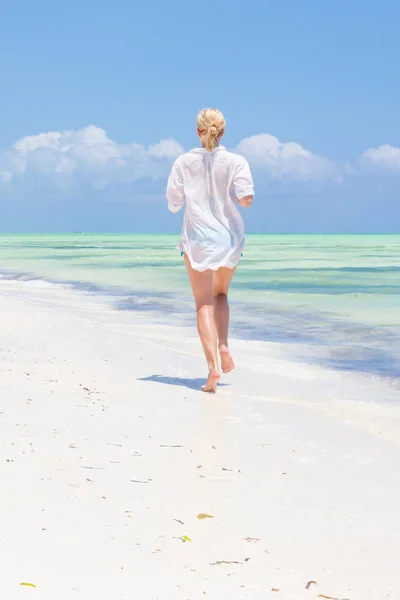 Mujer feliz divirtiéndose, disfrutando del verano, corriendo alegremente en la playa tropical. Hermosa modelo caucásica con túnica de playa blanca en vacaciones en la imagen perfecta playa de Paje, Zanzíbar, Tanzania . — Foto de Stock