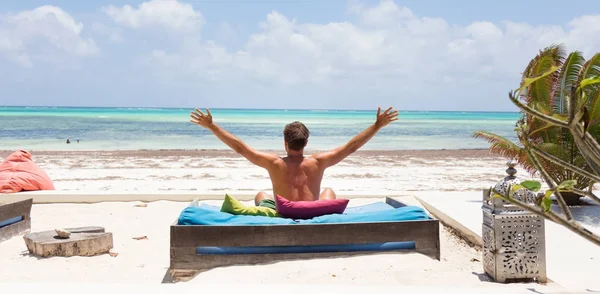 Relaxed man in luxury lounger, arms rised, enjoying summer vacations on beautiful beach. — Stock Photo, Image