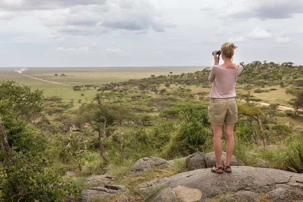 Female tourist looking through binoculars on African safari in Serengeti national park. Tanzania, Afrika. — Stock Photo, Image